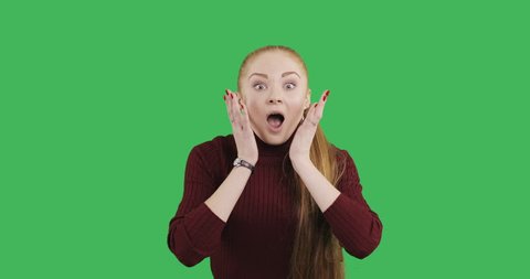 Female caucasian model with a long red hair is very surprised. Young woman with a great impression on green chroma key background.