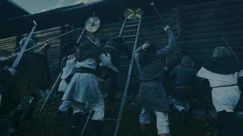 Large-Scale Medieval Battle Reenactment. Violent Tribe of Warriors Attack Wooden Fortress Wall, They Climb Ladders, Guards Try to Defend Fortification.They Fight with Axes, Swords, Spears, Bows.