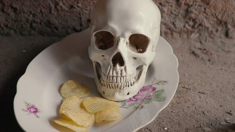 The concept of harmful junk food. Skull and falling chips. Slow motion.