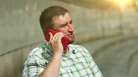 Man speaks on cell phone. Businessman communicates via smartphone. Fat sociable man in chequered shirt with red cell phone close-up