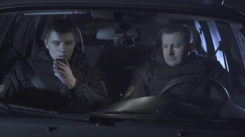 Two policemen are sitting in the car and answer the radio