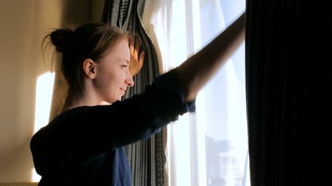 Happy woman opening curtains and looking out of window in cabin of cruise ship at morning