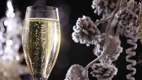 Christmas and New Year Champagne. Flute with Sparkling Champagne over Holiday Black Bokeh Blinking Background. Xmas Decoration. Decorated Xmass table setting. Celebrating. 4K UHD video, slow motion