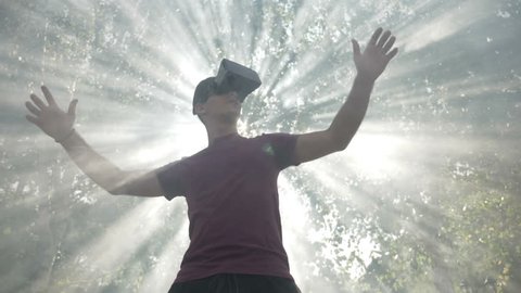 Young man with VR headset gadget immersed into virtual reality covered by light rays and waving smoke in slow motion 库存视频