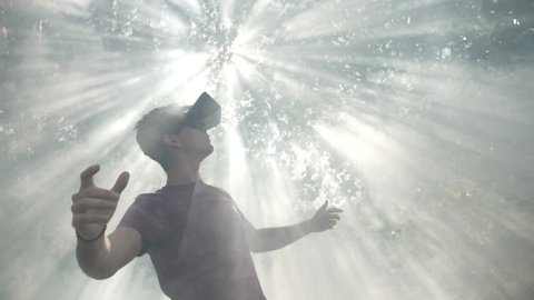 Excited millennial wearing virtual reality VR headset glasses feeling astonished by visual experience exploring cyberspace nature and sun in smoke slow motion