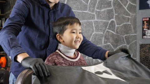 Barber covering the Asian child with a cloak, the child laughing 60 fps