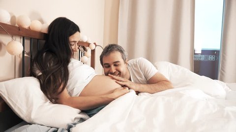 Handsome man and his pregnant wife spending time together in bed at home