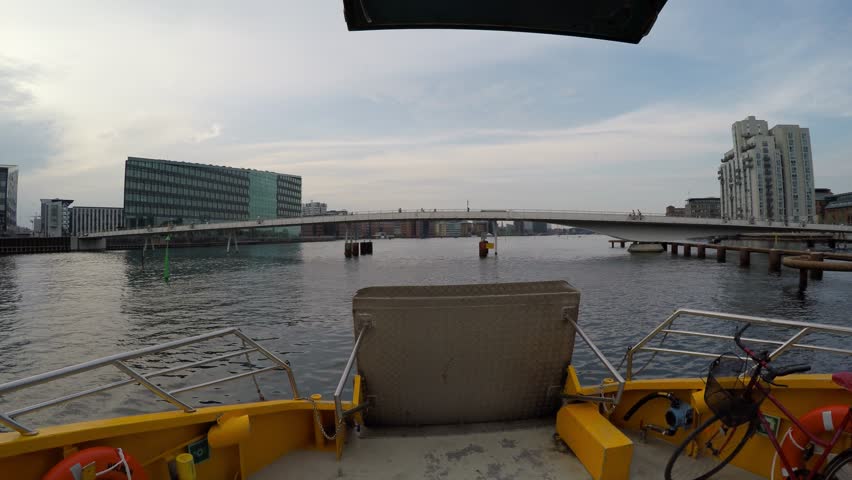 A ferry water taxi on the river in Copenhagen, Denmark, passes under a bridge with cyclists on bicycles
