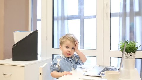 Portrait of child businessman in office playing with documents at home kids office. Successful confident business kid. Child humor, baby jokingly works behind a computer, throws out papers and falls