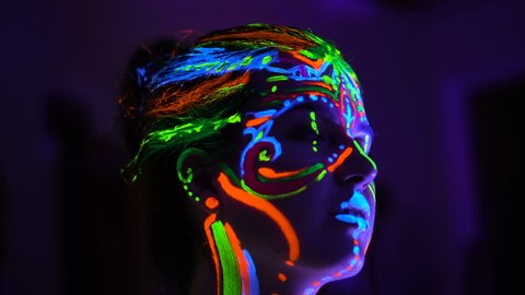 The bodyart ultraviolet painter draws on the face of Beautiful young sexy girl close up