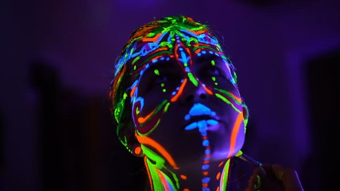 The bodyart ultraviolet painter draws on the face of Beautiful young sexy girl close up