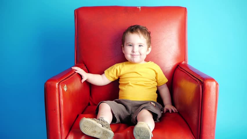 boy sitting in a red chair and waving