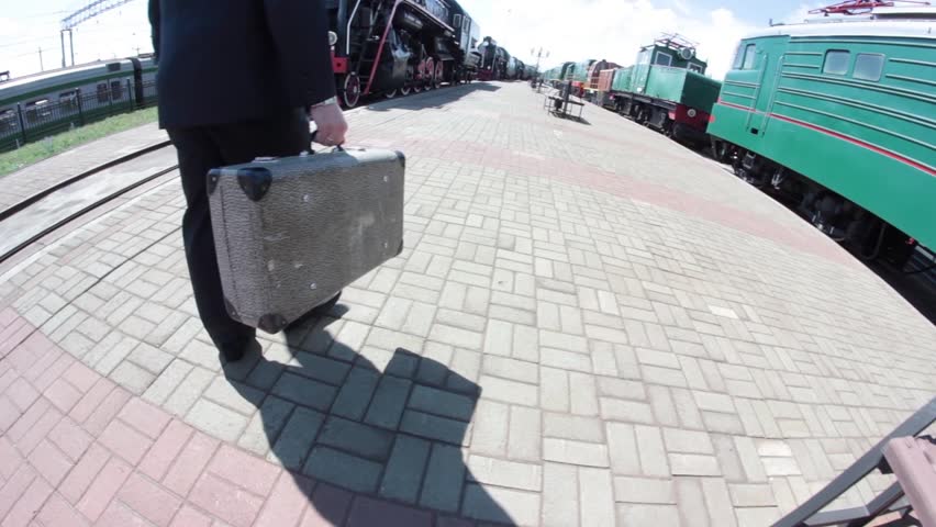 man walking on a railway station with a grey suitcase