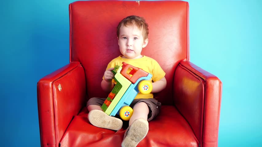 a kid playing with toy truck in red chair