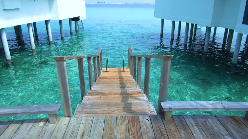 Walk on the wooden ladder to turquoise water among water bungalows in day time.