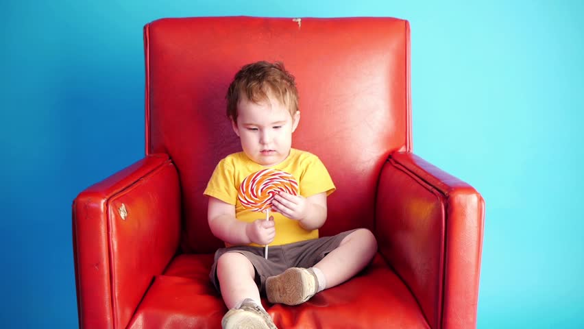a kid sitting in red chair holding big candy