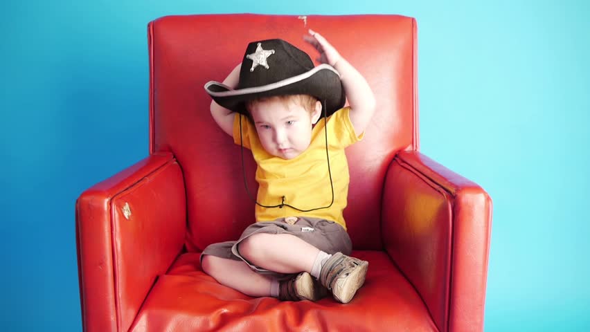 little boy in officers hat sitting in red chair