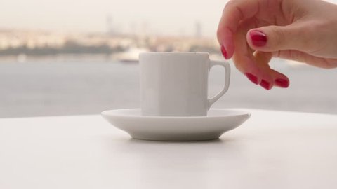 Tourist woman enjoy traditional hot Turkish drink at panoramic terrace, hand take small cup of coffee, nice blurred background, silhouetted Bosphorus Strait panorama. Lady take gulp and place cup back