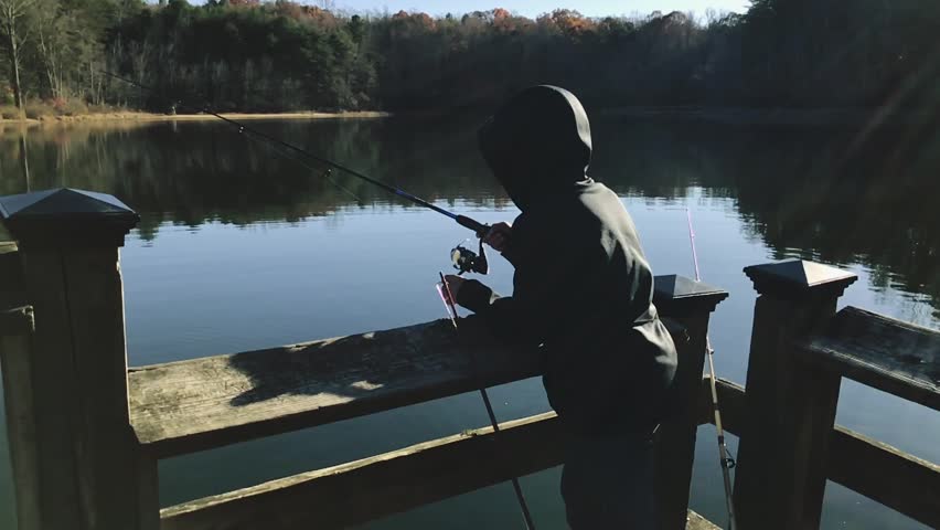 Slow motion shot from behind of a kid fishing on a lake and looking back