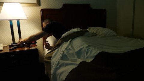 A man wakes up late at night in a hotel room and turns on the light