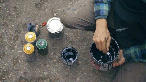 Close up shot of Artist who stir a black paint into a can and pouring it to another can on the ground. View from top