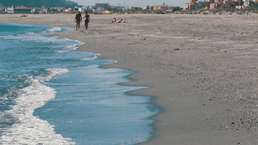 A young couple walks along the shores of the Mediterranean Sea against the background of the Rock of Gibraltar, enveloped in hot yeast air