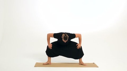 Man demonstrates stretching exercises on a yoga mat against a white background. He is showing a version of parivrtta utkatasana / twisted chair pose.
