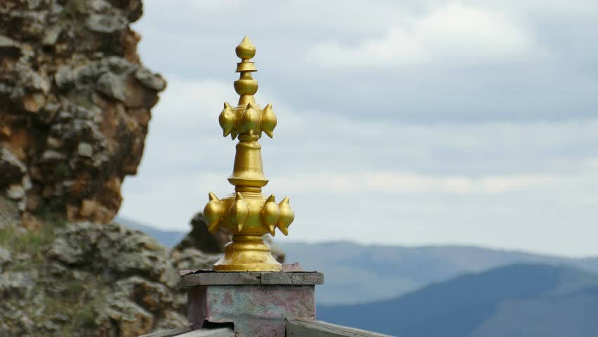 Golden decoration of a Buddhist temple against a cliff and a picturesque cloudy sky. 