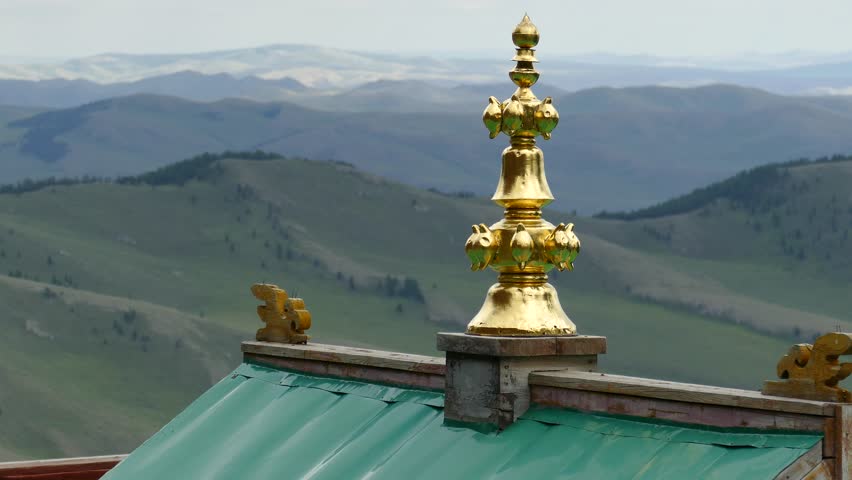 Golden decoration of a Buddhist temple against a picturesque mountains and a cloudy sky. 
