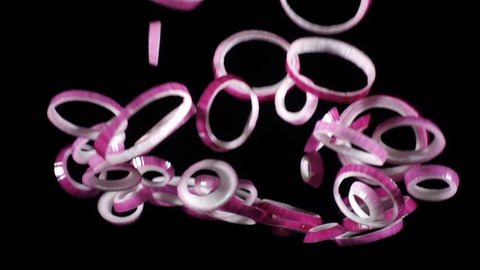 Falling rings of red onion slices isolated on black background, slow motion