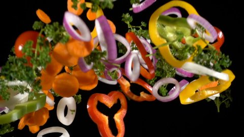 Falling cuts of plenty colorful vegetables isolated on black background, slow motion