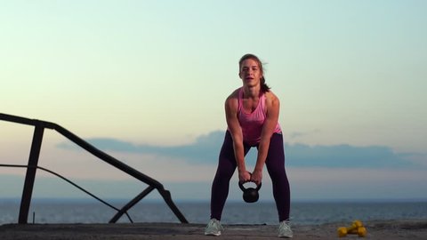Slow Motion - Sportswoman Wearing Sportswear Doing Kettlebell Swings Exercise Outdoors. Fitness Female Working Out on the Beach at Sunset. Athletic Young Woman is Engaged in Outdoor Sports.