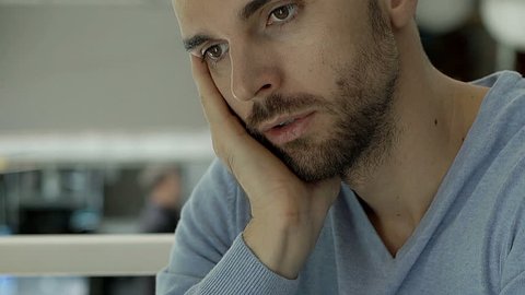 Handsome man in blue sweater sitting on the balcony in the cafe and looks worried, steadycam shot

