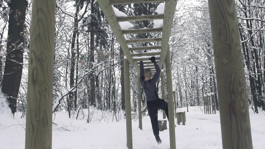 Slow Motion Of Young Sportsman Training On Horizontal Ladder In Snowy Forrest.