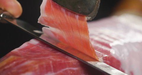 Close up macro of a chef who cuts a slice of ham, of excellent quality, with the knife according to tradition. Concept of: ham, food, Spain and Italy, catering.
