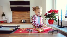 Video of pretty little girl with funny pigtails baking Christmas cookies of different forms in modern kitchen