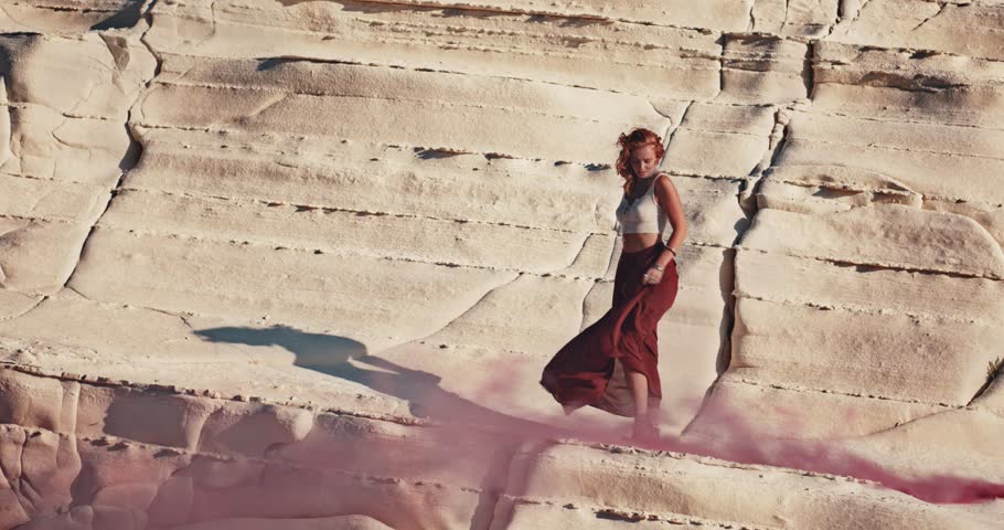 Young boho woman at desert music festival standing on rock and partying with smoke bombs