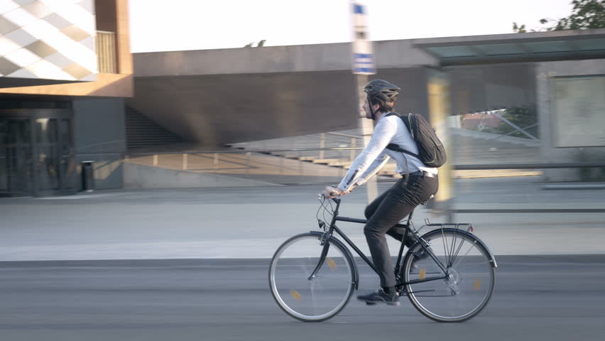 Businessman wearing formal clothes riding a bike on his commute. Elegant handsome young professional travelling to job on a bicycle on the street in the city.