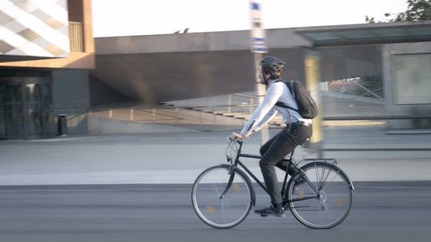Businessman wearing formal clothes riding a bike on his commute. Elegant handsome young professional travelling to job on a bicycle on the street in the city.