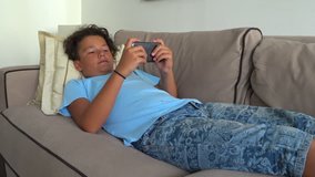 Preteen boy laying sofa with smartphone texting message or playing game at home. Technology, internet communication and people concept