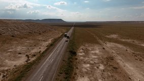 Aerial footage of vehicles moving on highroad in desert environment to developing logistic and transportation.Video of trucks and cars with cargo driving on asphalt way of dry wild lands