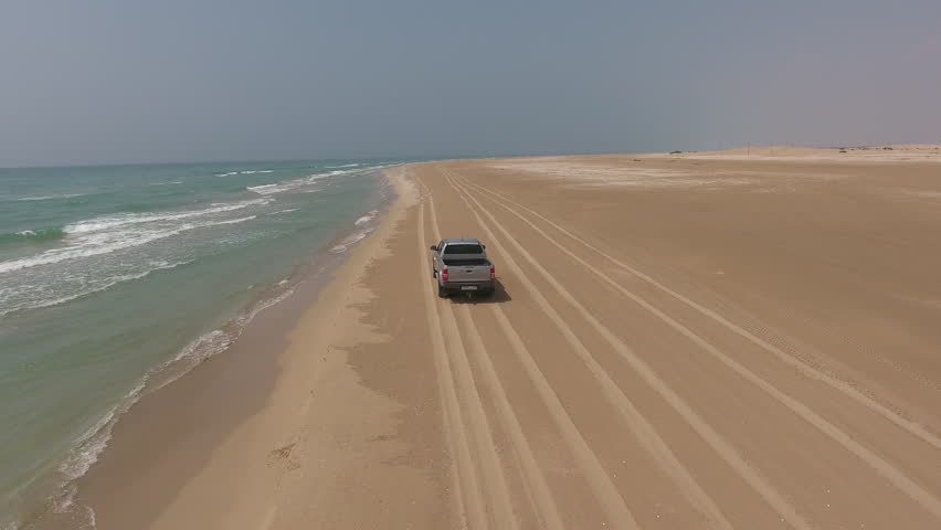Aerial video trip of rented car driving along sandy beach washed by ocean waves.Footage of travelers having extreme vehicle adventure on seashore during summer journey