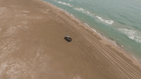 Aerial footage of rented jeep crossing sandy dry land near sea during summer holiday.Bird’s video of motor car with speed driving on off road on seashore 