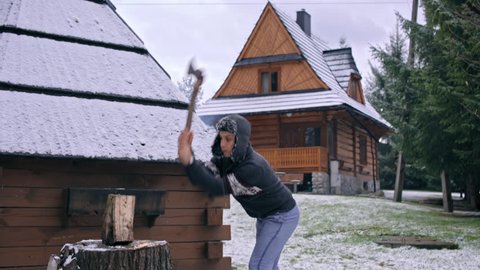 Slow Motion of a Handsome Young Man Splitting Logs with Axe near House in Winter
