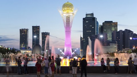 Bayterek Tower and fountain show day to night timelapse. People walking around. Skyscrapers on background. Bayterek is a monument and observation tower in Astana. Astana, Kazakhstan