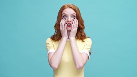 Shocked happy young ginger woman in dress saying omg and looking at the camera over blue background