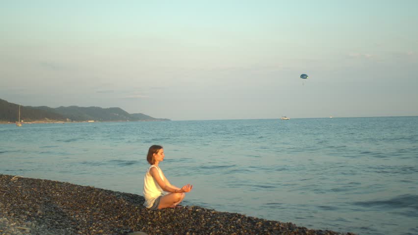 Young woman meditating by the sea at sunset