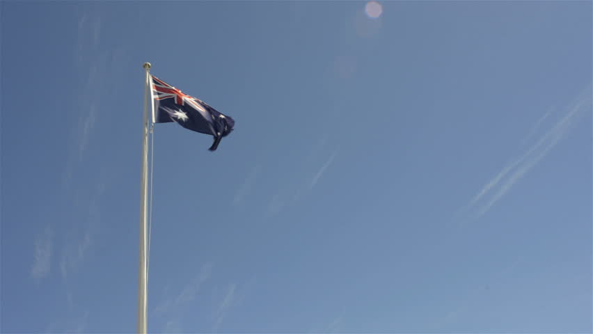 An Australian flag flying and flapping in the wind, with lots of blue sky.
