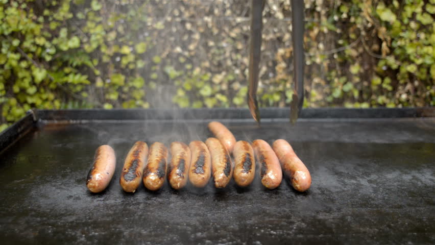 Sausages being cooked on a BBQ, with a hand coming in to turn them over with