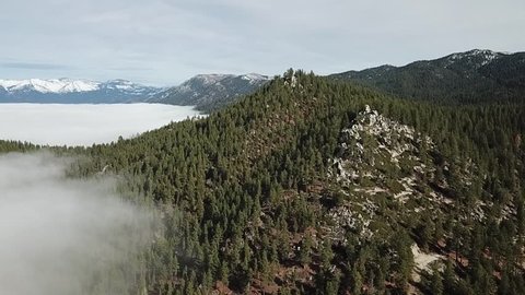 drone flys over forest with a mountain in the right of the frame. fog fills the left side of the frame creeping into the trees and filling the lake. camera rotates slightly to the left